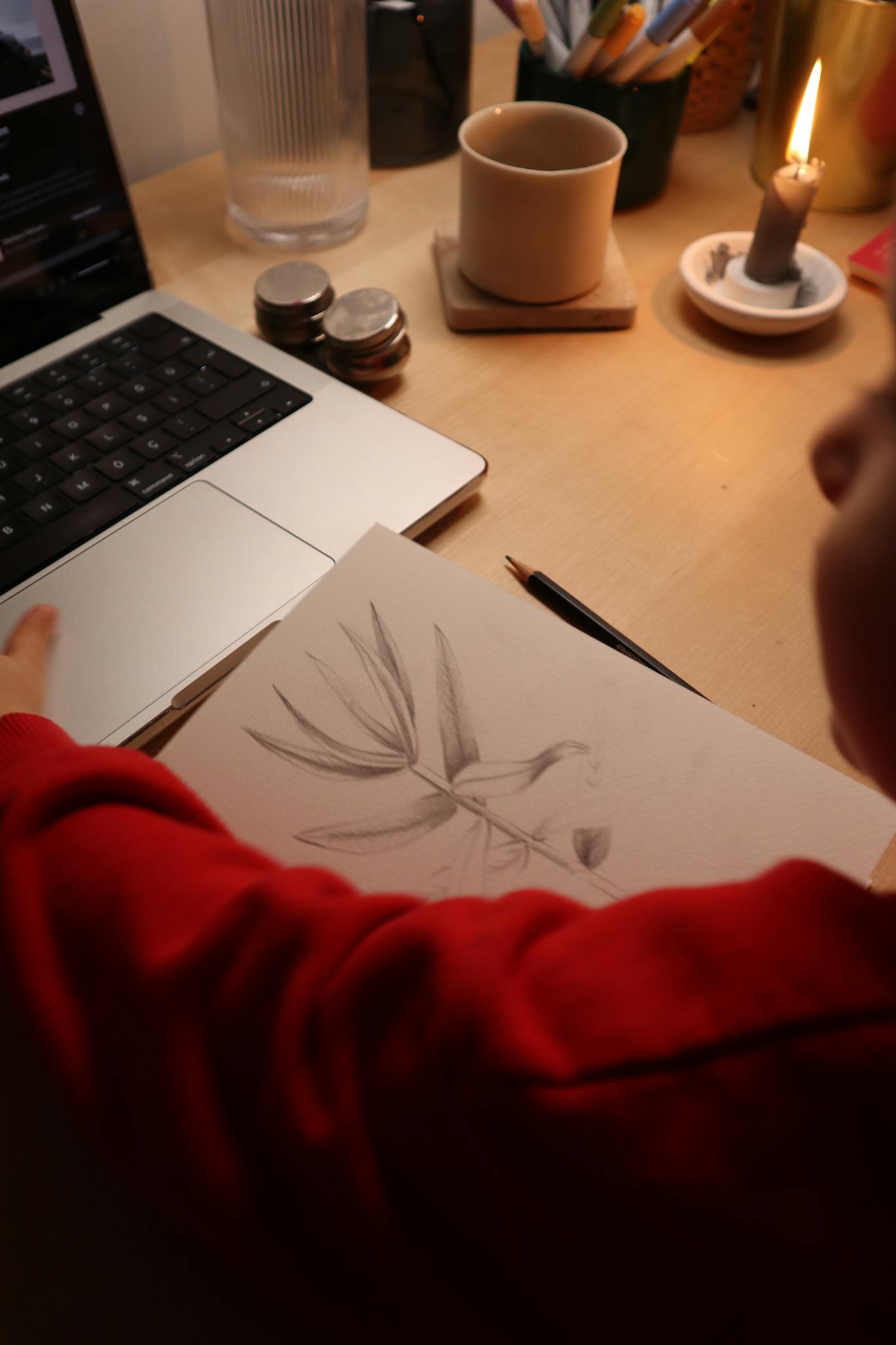 A cozy workspace featuring a drawing pad, laptop, and candlelight ambiance.
