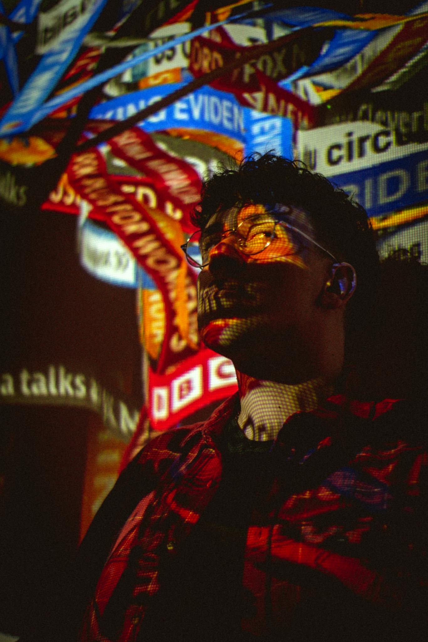 A man stands illuminated by colorful projections, creating a modern artistic scene.